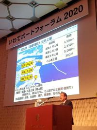 いわてポートフォーラム2020と書かれた横断幕の下のスクリーンに映し出された 宮古港のPRを市長が演台で話している写真