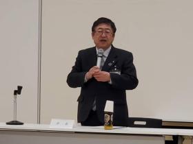 市長と書かれたネームプレートの席で立ち、今年度の実績と来年度の計画について、 報告している写真