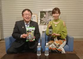 市長とフリーアナウンサーの塩地美澄さんがそれぞれ番組で紹介した商品を持って、 椅子に座って撮影した写真