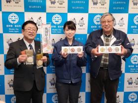 丸友しまか有限会社の2人が商品の箱を持ち、市長が個別包装された商品を持って 並んで撮影した写真