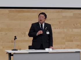 市長が会議の自席で立ちながらマイクを片手で持ち防災計画と水防計画の修正案について述べている写真