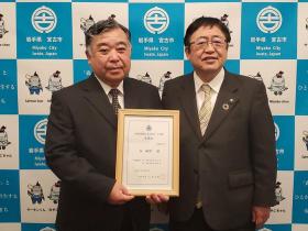 第8号PR隊員の谷敏明さんが承認証を持ち、市長と並んで撮影した写真