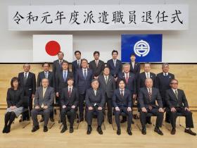 令和元年度派遣職員退任式と書かれた横断幕の下で、退任される7人の方と関係部署の方々、市長を含めて計20人が並んで撮影した写真