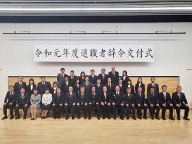令和元年度退職者辞令交付式と書かれた横断幕の下で、退職される方々が整列して撮影した写真