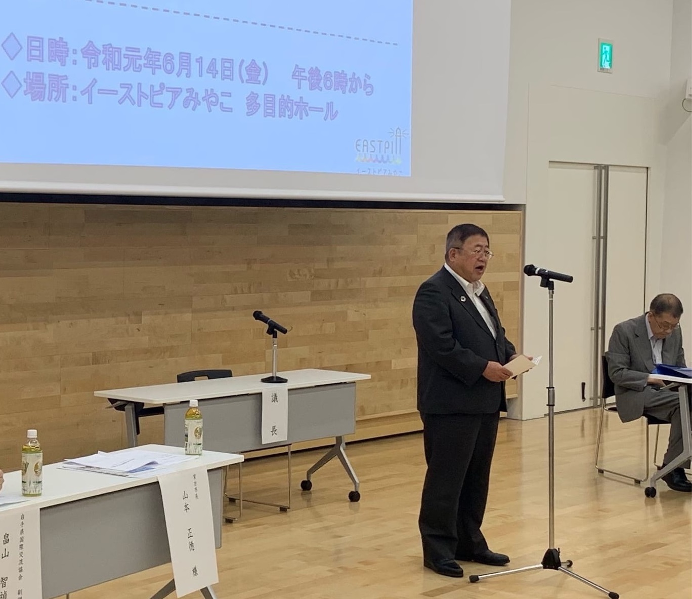 画面が映されたスクリーンの前方に置かれたスタンドマイクに向かい話をする様子の市長の写真