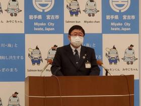宮古市のバックパネルの前で、演台に置かれたマイクに向かい話をする様子の市長の写真
