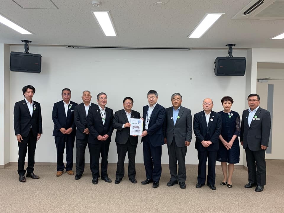 両端の天井にスピーカーが設置された室内で、岩手河川国道事務所の代表の男性と市長が一緒に要望書を持ち他8名の関係者が横一列に並んでいる写真