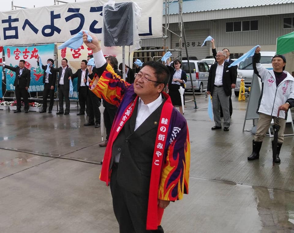 「宮古へようこそ」と大きく書かれた宮古港で、寄港した客船「ぱしふぃっくびいなす」の出港を法被を着た市長や関係者の方々が水色のハンカチを振ってお見送りしている様子の写真