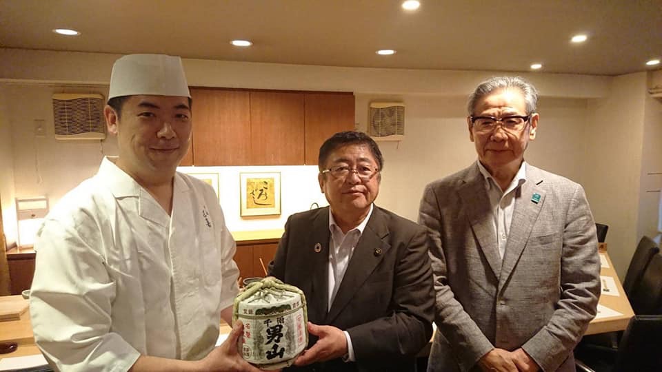 カウンターの席の前で、本州最東端のまち宮古・PR隊に承認された吉村匡史さんと市長が小さな樽酒を一緒に持ち、1名の男性と横一列に並んでいる写真