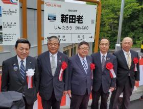 「新田老」と書かれた駅名標の前で、胸章を着けて横一列に並ぶ市長と4名の関係者の男性の記念写真