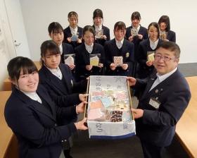 手作りマスクが入った箱を持つ2名の女子生徒と市長、その後方で1枚ずつマスクを持つ8名の女子生徒が写った記念写真