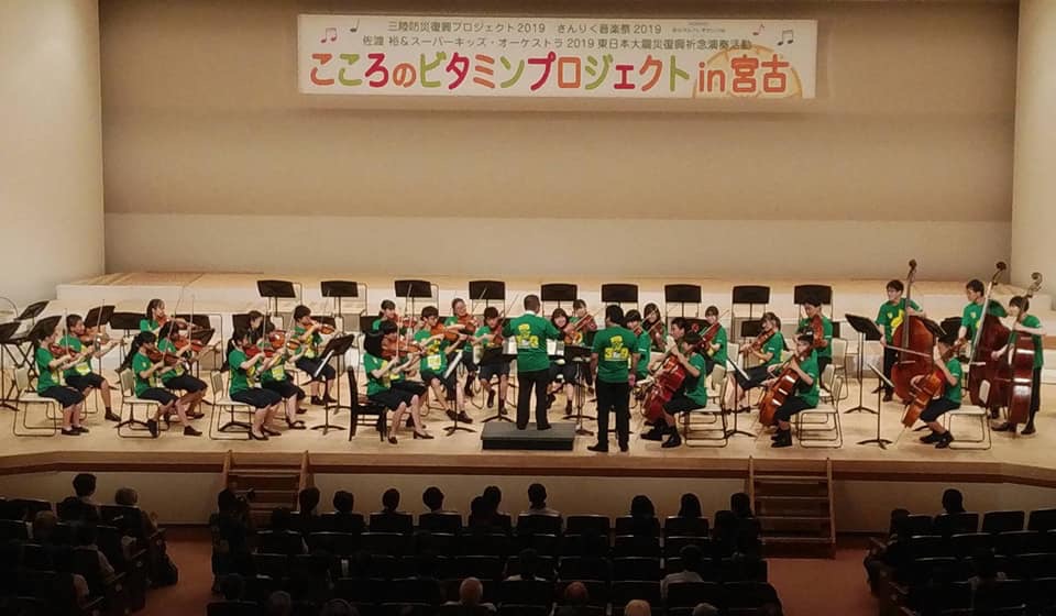 舞台上で演奏する様子のスーパーキッズ・オーケストラの方々の写真