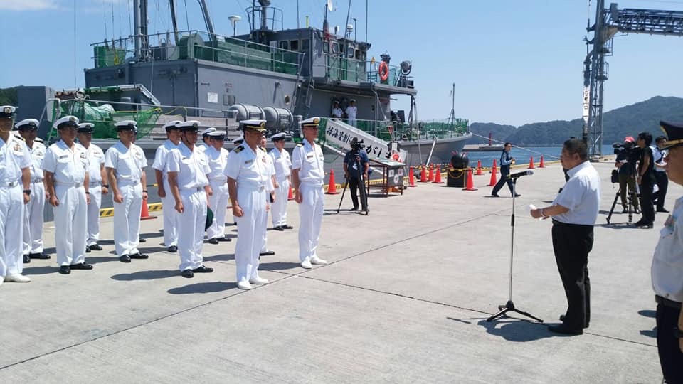 海上自衛隊掃海管制艇「ながしま」の前で整列する白い制服を着た自衛隊員たちと、その向かい側でスタンドマイクで話をする市長の写真