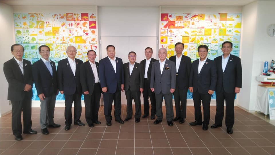 カラフルな色で制作された2枚の大きなデザイン画が設置された壁をバックに、岩手県市長会議に参加された11名の各市長の方々が横一列に並んでいる記念写真