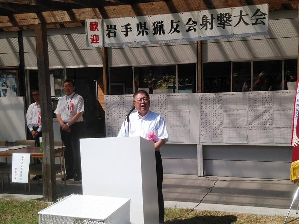 「歓迎 岩手県猟友会射撃大会」と書かれた横断幕が掲げられた屋外の檀上で、開会式の挨拶を行っている市長の写真