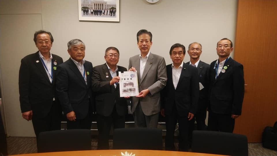 絵画と時計が壁に飾られた室内で、中央に公明党の山口那津男代表と若松謙維参議院議員と市長が一緒に要望書を持ち、5名の関係者が横一列に並んでいる写真