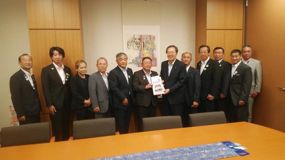 大きなテーブルが設置された室内で、中央に斉藤鉄夫幹事長と市長が一緒に要望書を持ち、10名の関係者が横一列に並んでいる写真