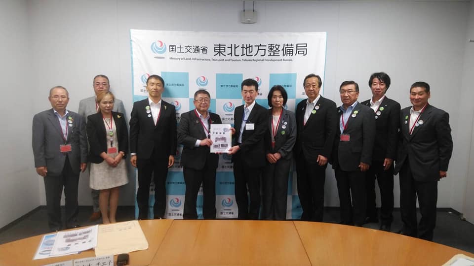 国土交通省東北地方整備局と書かれたバックパネルの前で、中央に東北地方整備局の佐藤克英局長と市長が一緒に要望書を持ち、9名の関係者が横一列に並んでいる写真