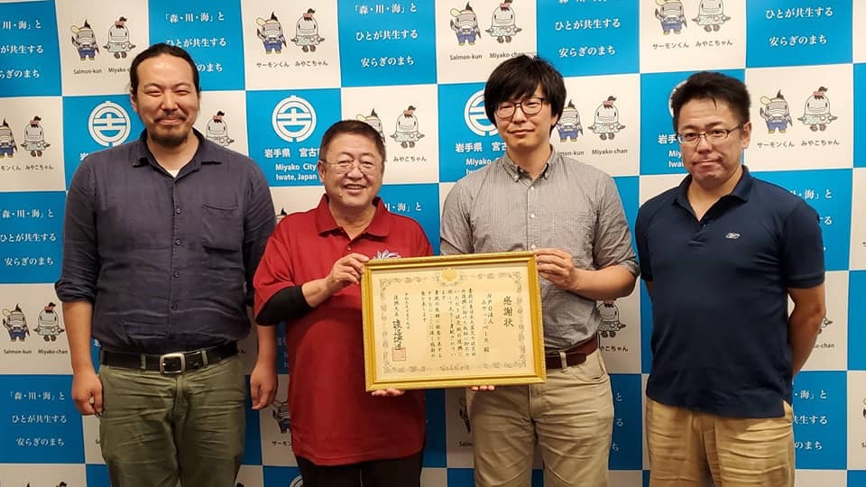 バックパネルの前で感謝状を一緒に持つ市長と男性1名、両側に立つ男性2名を写した記念写真