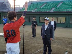 野球場で帽子を被った市長に、赤いユニフォームの代表選手が選手宣誓をしている写真