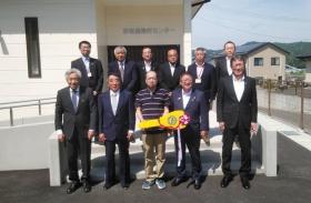 赤前農漁村センターの入口で1人が紅白のリボンがついた黄色の大きな鍵のレプリカを持ち、市長の他、関係者10人が並んで撮影した写真