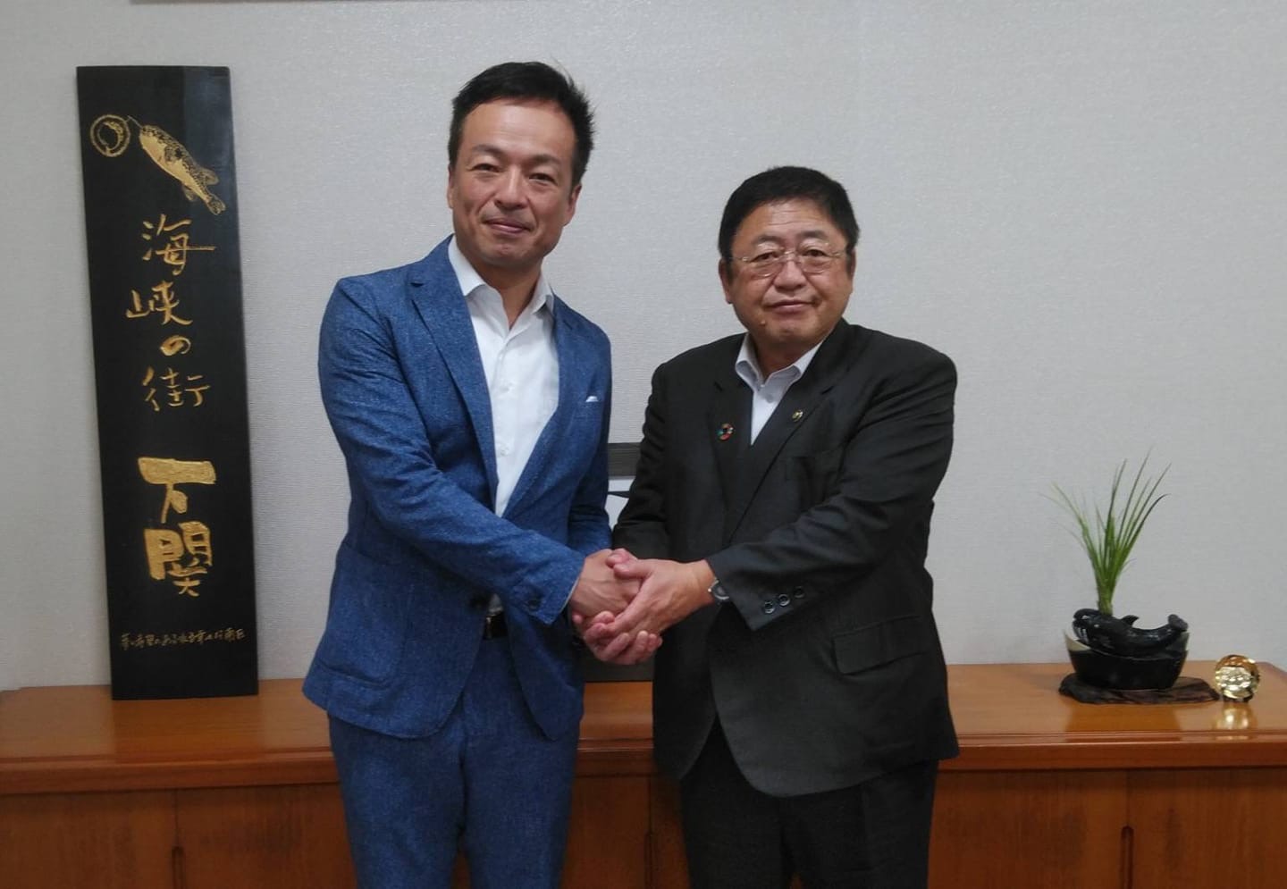 両手で握手をして体を正面に向けている市長と下関市の前田晋太郎市長の記念写真