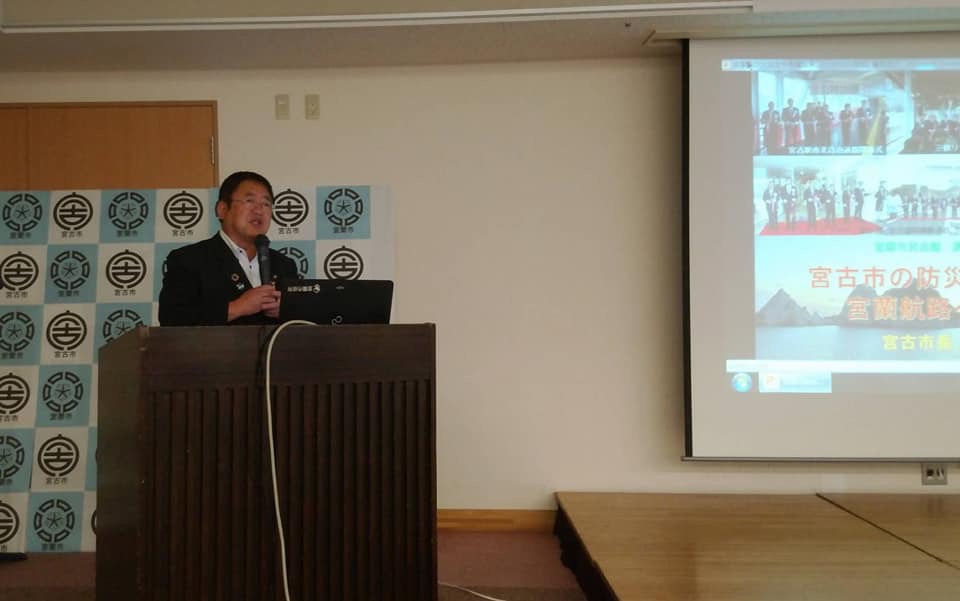 画面が映されたスクリーンの横に置かれた演台で、右手にマイクを持ち話をしている市長の写真