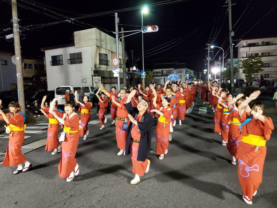 黒い法被を着た市長含む赤い着物の方々が4列になって踊りながら歩いている様子の写真
