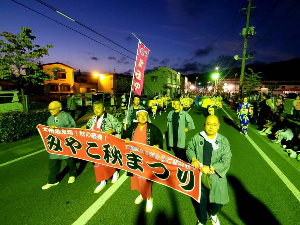 みやこ秋まつりとかかれた横断幕を持った市長らを先頭に黄色の浴衣を着た女性など長い列を成して踊りながら歩いている様子の写真