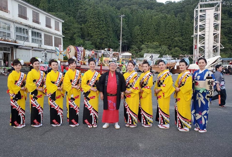 赤い着物に黒の法被を着た市長を中心に、お揃いの黄色の着物とタスキを付けた9名の女性と青い着物に「秋まつり」と書かれた提灯を持った女性が並んでいる写真