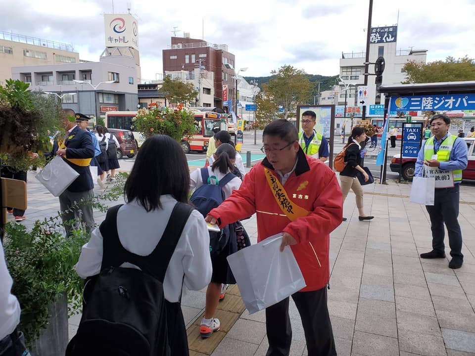タスキを付けた市長が街頭で学生にポケットティッシュを手渡している様子の写真
