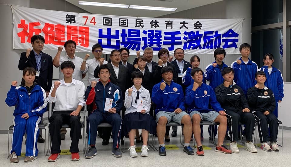 出場選手激励会の横断幕の前に、出場選手や関係者20名程が並んでガッツポーズをしている集合写真