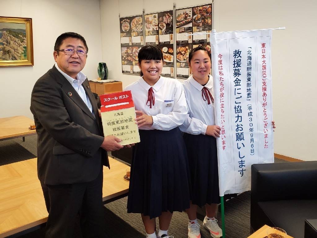 市長と女子生徒が2人で募金箱を持ち、もう一人の女子生徒が募金協力の旗を持っている写真