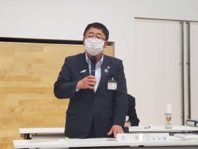 市長が会長と書かれたネームプレートの席で立って、事業計画や 収支予算案などについて述べている写真