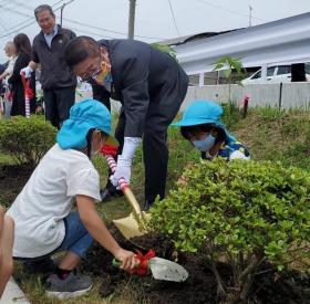 市長が青い帽子を被った磯鶏保育所園児の2人とツツジを植樹している写真