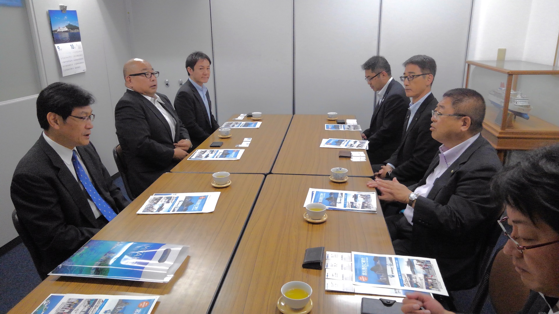 並べられた茶色い長机に向かい合うようにして座る市長と6名の関係者の写真
