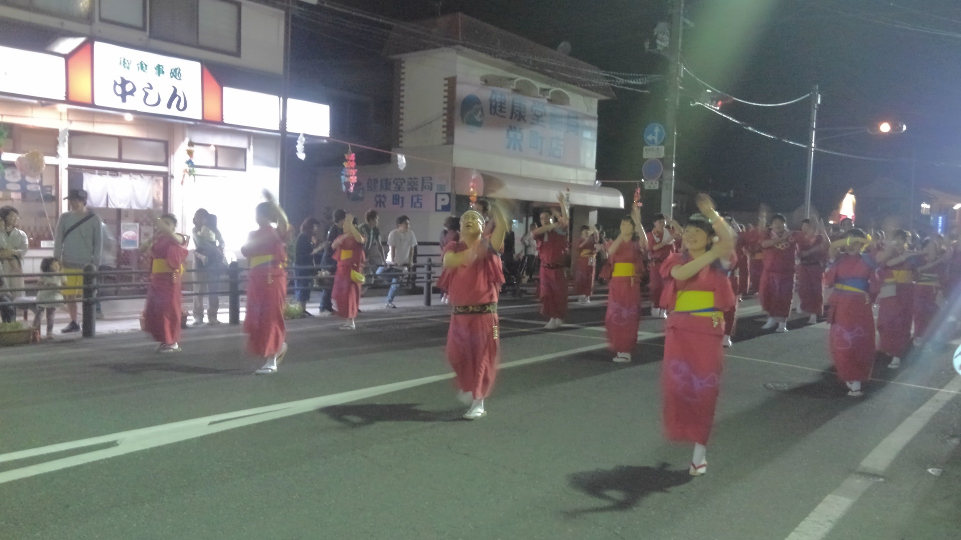赤い着物を着て踊りながら道路を進む様子の参加者たちの写真