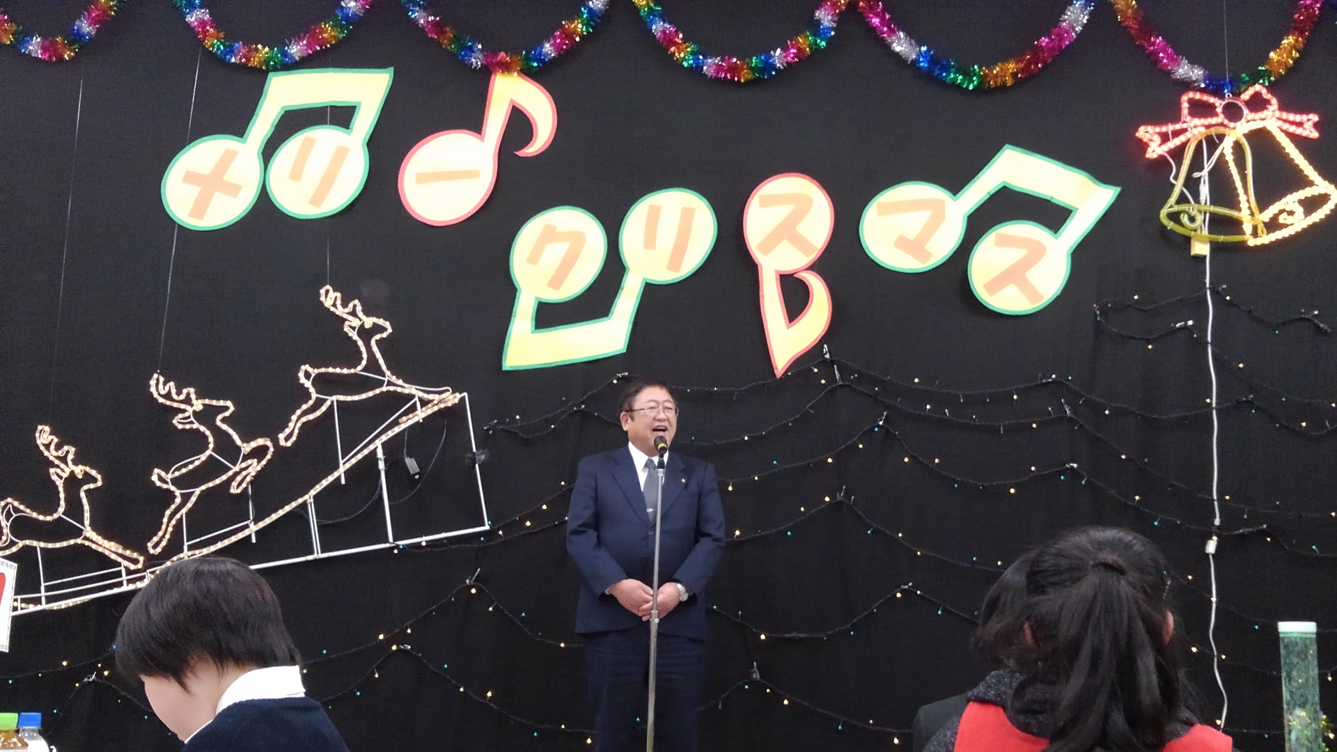 クリスマスの装飾が施された黒い壁の前で、スタンドマイクに向かい話をする様子の市長の写真