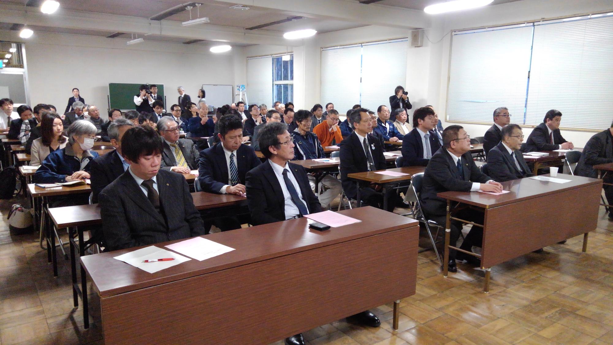 並べられた長机の席に着席している大勢の参加者たちの写真