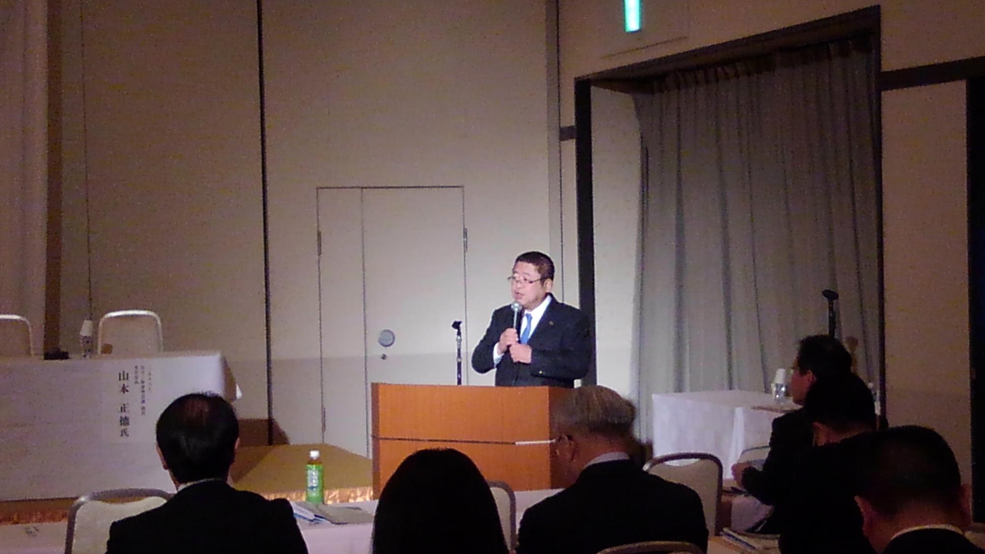 演台で両手にマイクを持ち話をする様子の市長の写真