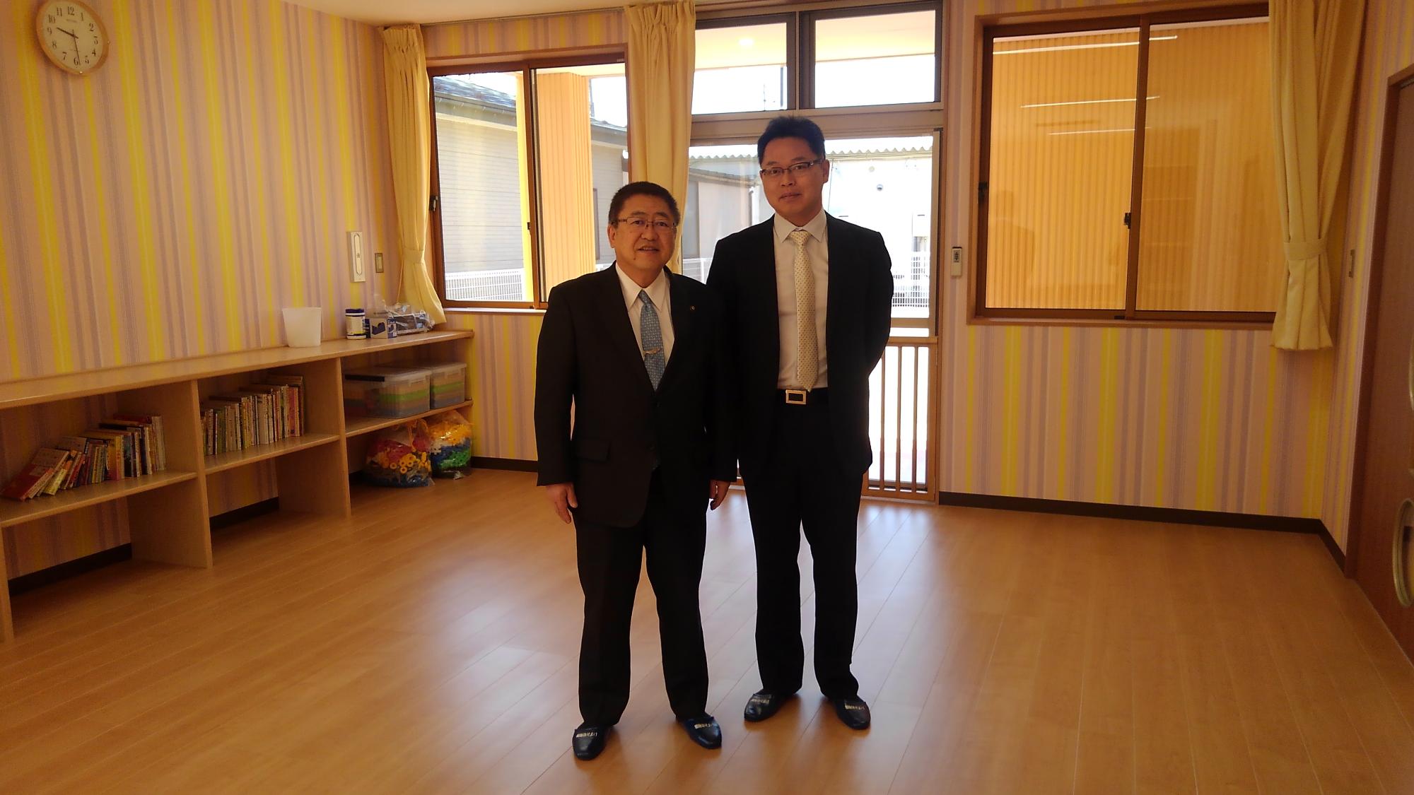 フローリングの床の部屋の中で横並びに立っている市長と男性の記念写真