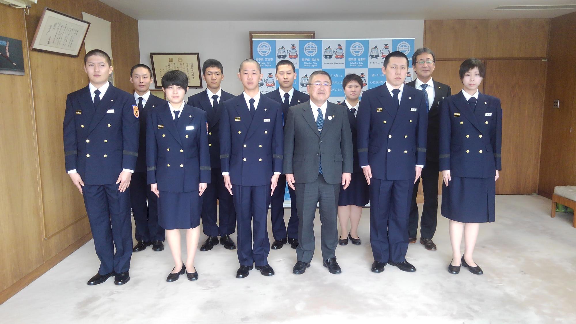 制服を着て立つ新採用消防職員の方々9名と市長、関係者の男性1名が2列に並ぶ記念写真
