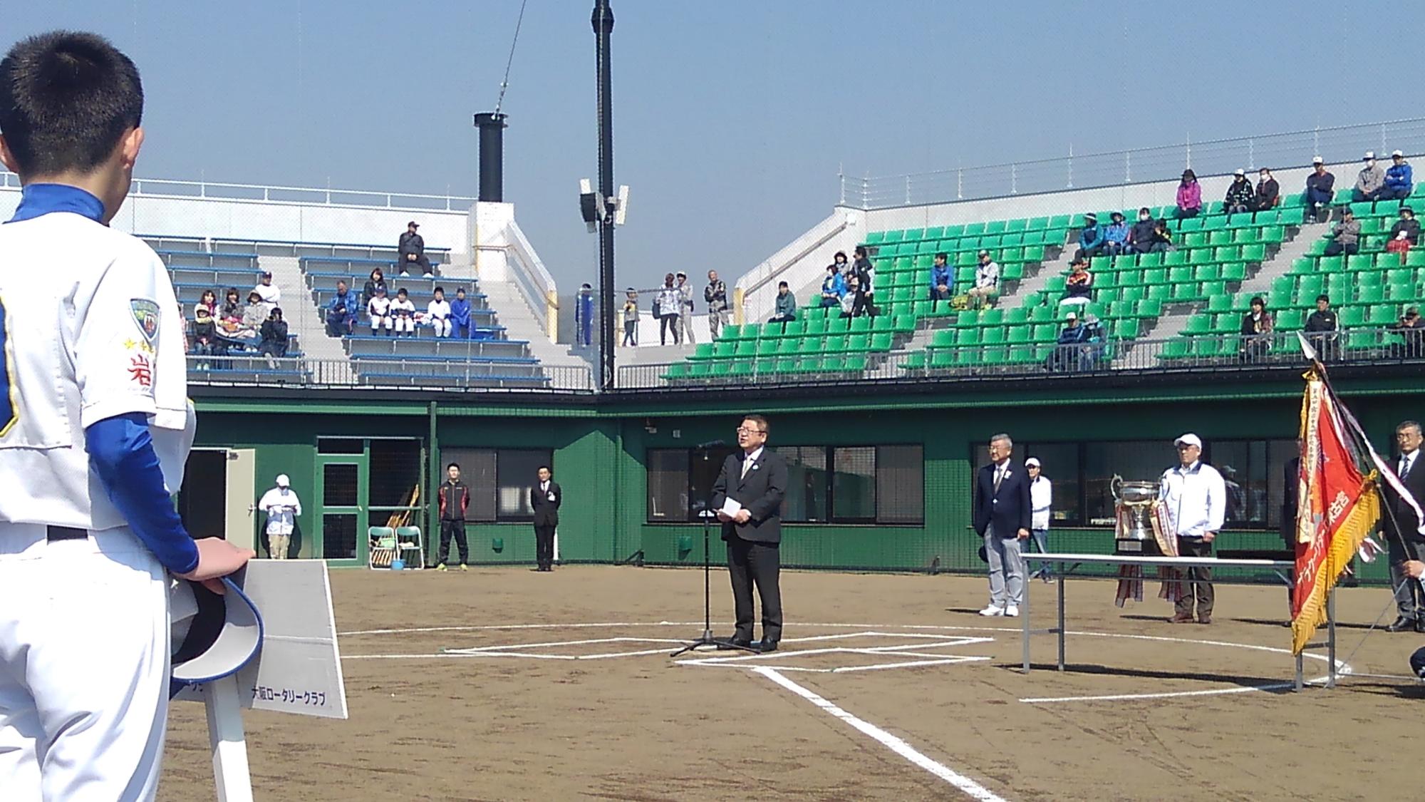 野球場のホームベースに置かれたスタンドマイクに向かい話をする様子の市長の写真
