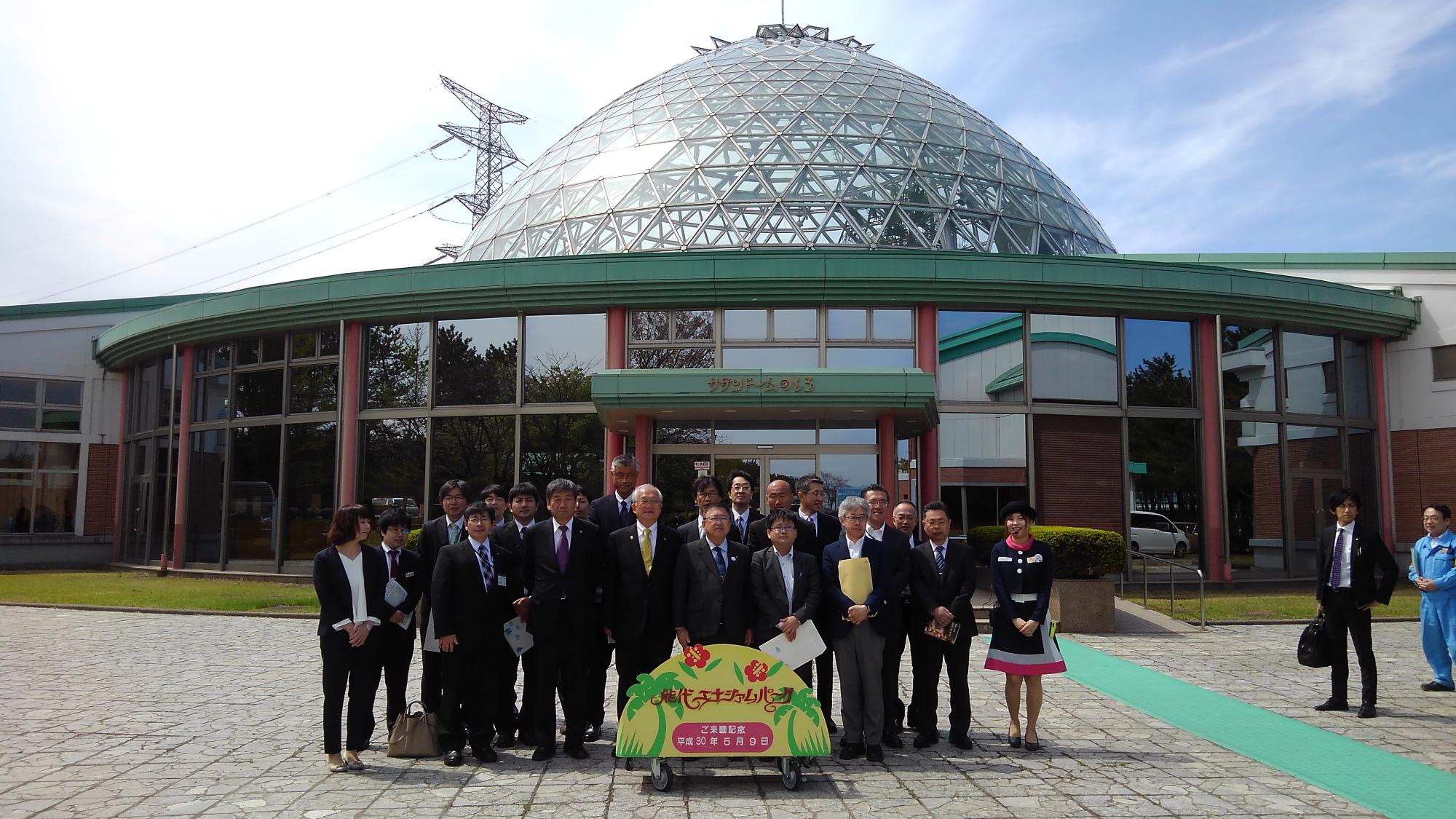 ガラス張りのドームのような形の建物の前で、3列に並び記念撮影をする市長と関係者の方々の写真