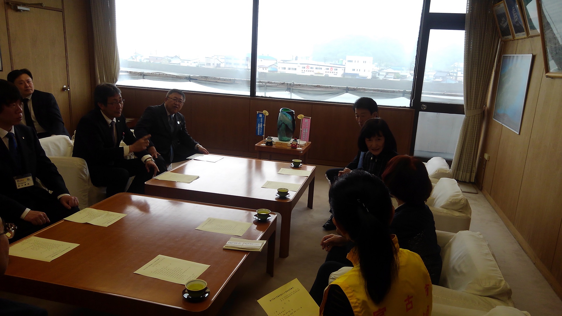 2台の茶色いテーブルの両側に置かれた白い椅子に向かい合うように座る市長と関係者の方々の写真