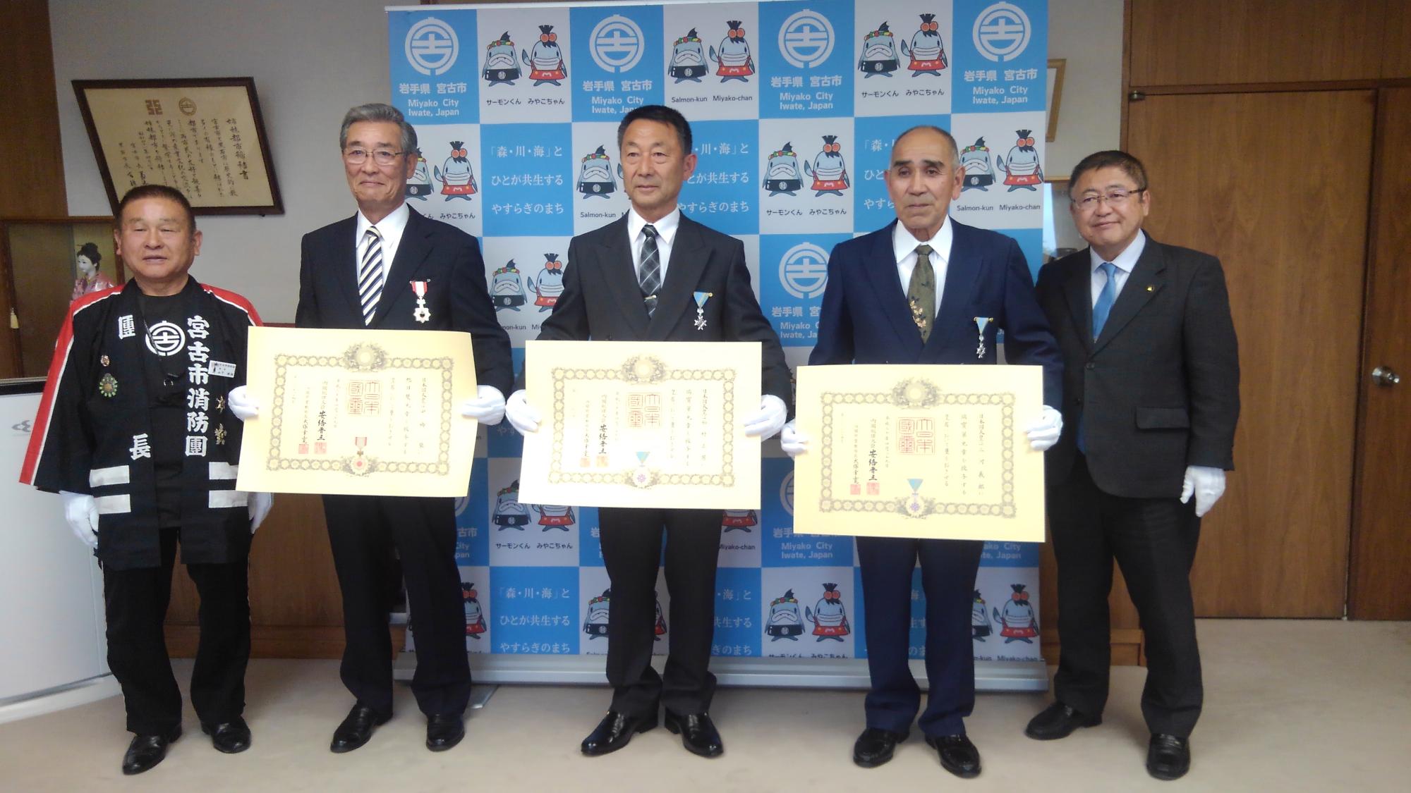 賞状を持つ3名の男性を中心に、法被を着た男性と市長が横一列に並んでいる記念写真