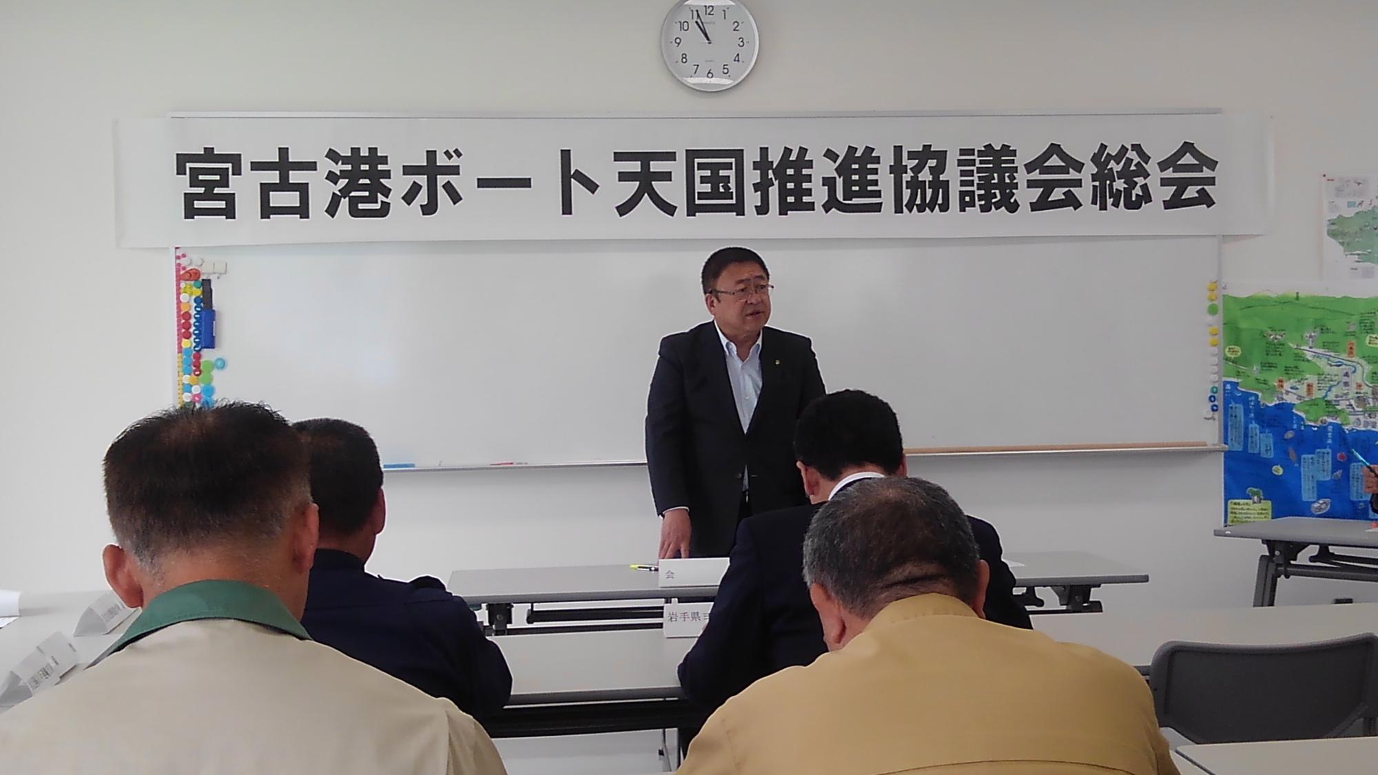 「宮古港ボート天国推進協議会総会」と書かれた横長の紙が貼られたホワイトボードの前で、立って話す市長と、席に着き下を向いて話を聞く様子の4名の参加者の写真