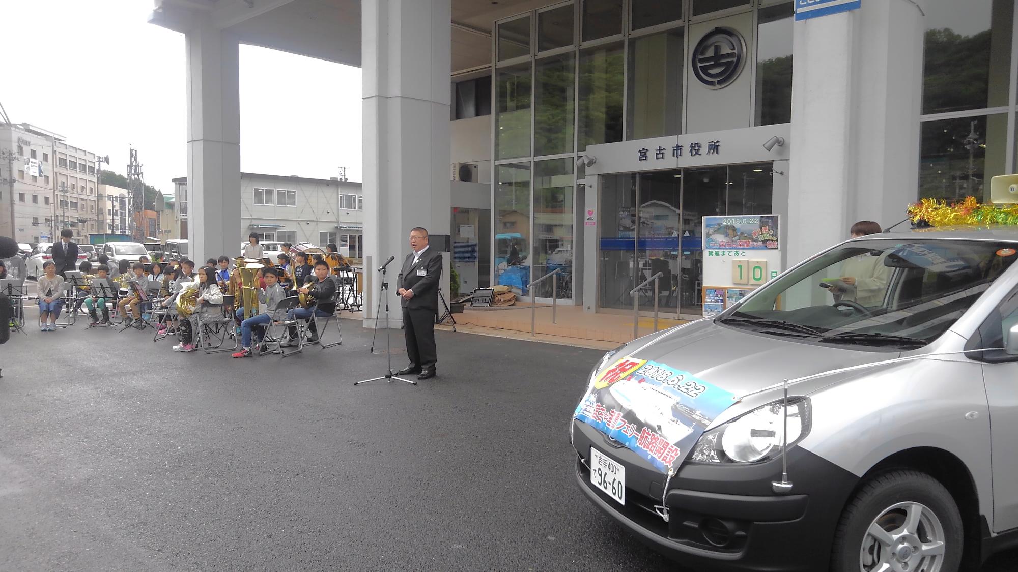 宮古市役所の入り口の前で、スタンドマイクに向かい話をする様子の市長の写真