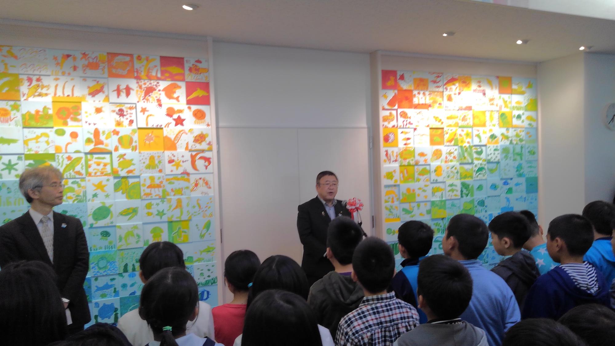 紅白リボンがつけられたマイクに向かい話をする様子の市長と、向かい側で整列して話を聞く子供たちの写真