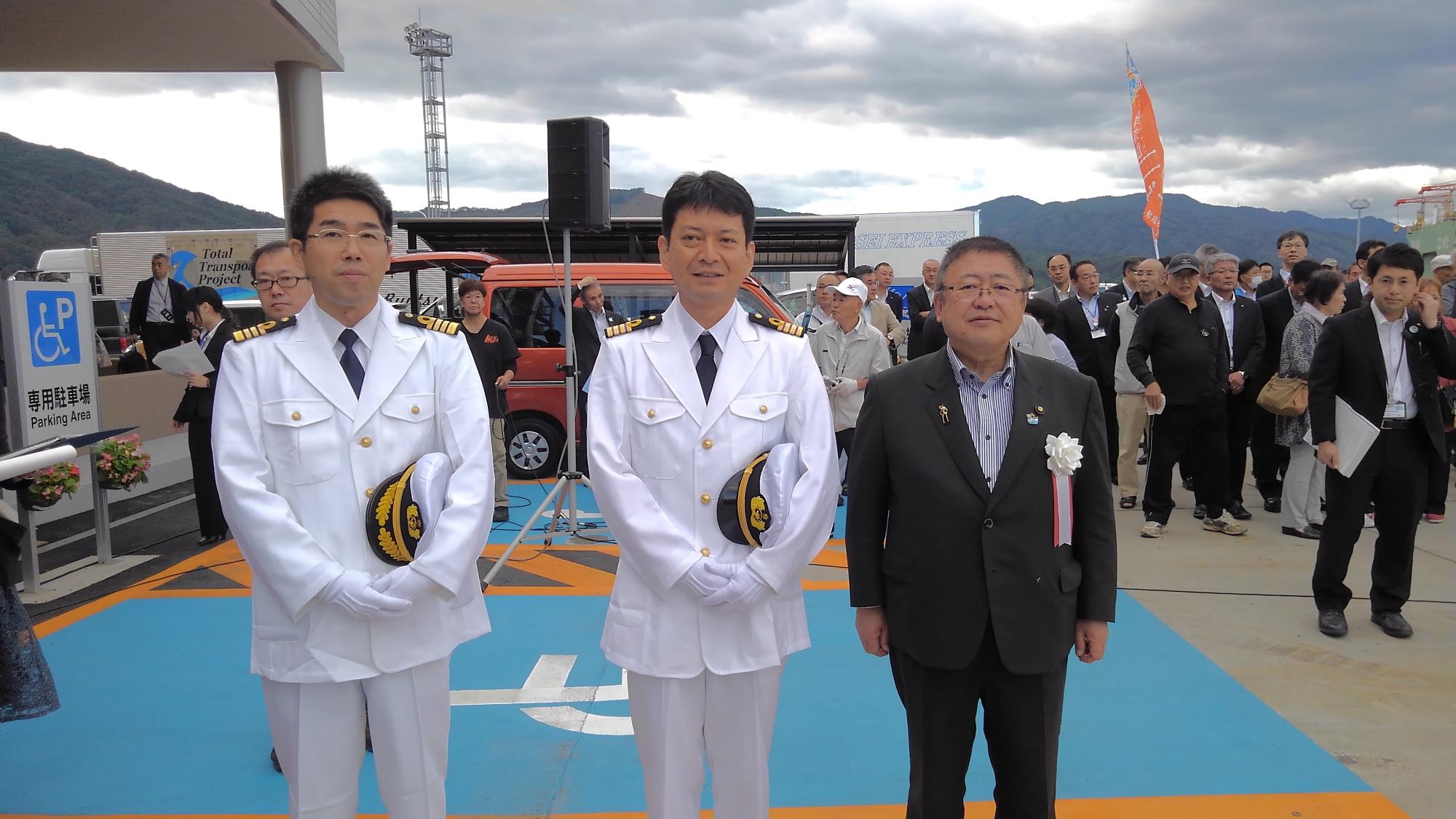 白い制服を着た乗組員2名と市長が並んで立つ記念写真